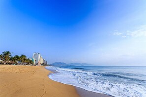 Uma praia com céu claro, areal arenoso e edifícios ao fundo.