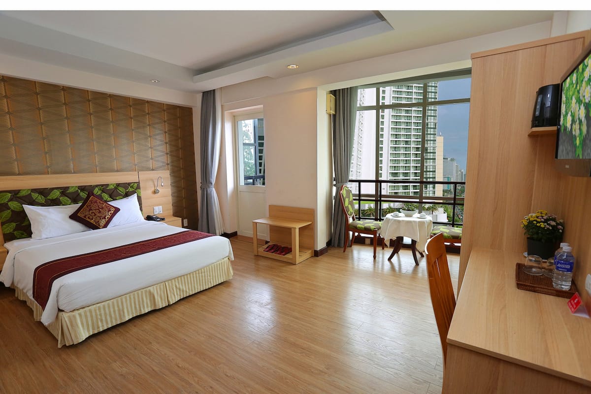 Habitación de hotel con una cama grande, un escritorio, una silla y vistas a un paisaje urbano a través de un ventanal.