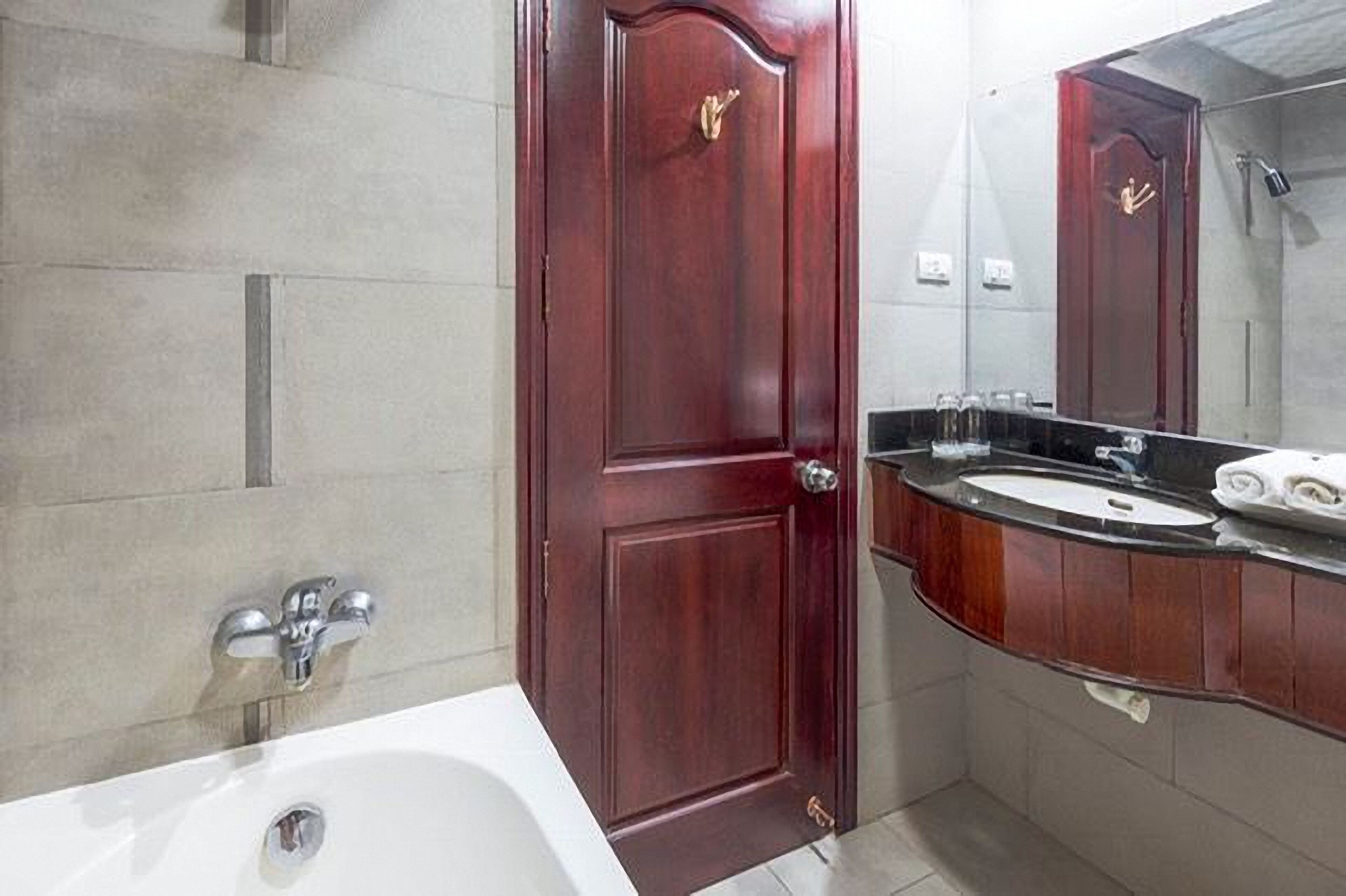 A bathroom with a white bathtub, a wooden door, a vanity with a mirror, and a towel rack.