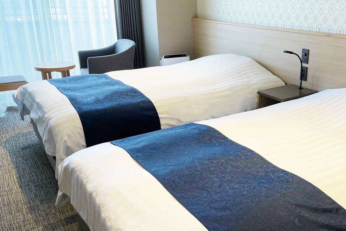 Habitación de hotel con dos camas, un escritorio, una silla y una mesita.