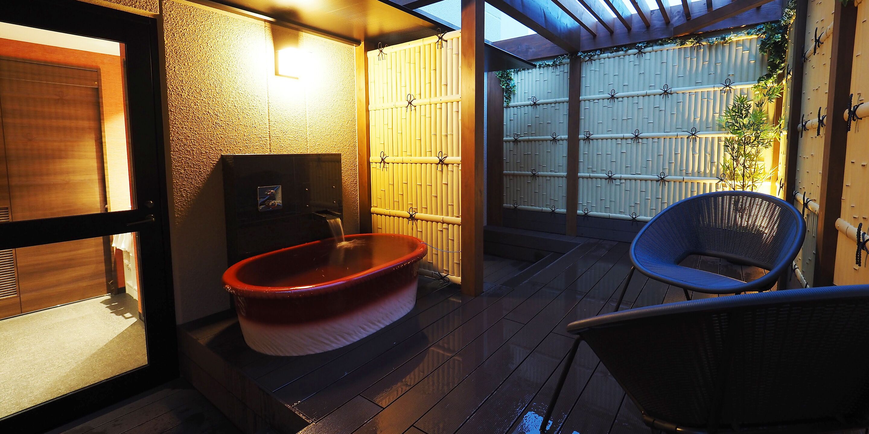 A traditional Japanese-style bathroom with a wooden bathtub, a bamboo fence, and a blue chair.