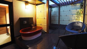 A traditional Japanese-style bathroom with a wooden bathtub, a bamboo fence, and a blue chair.
