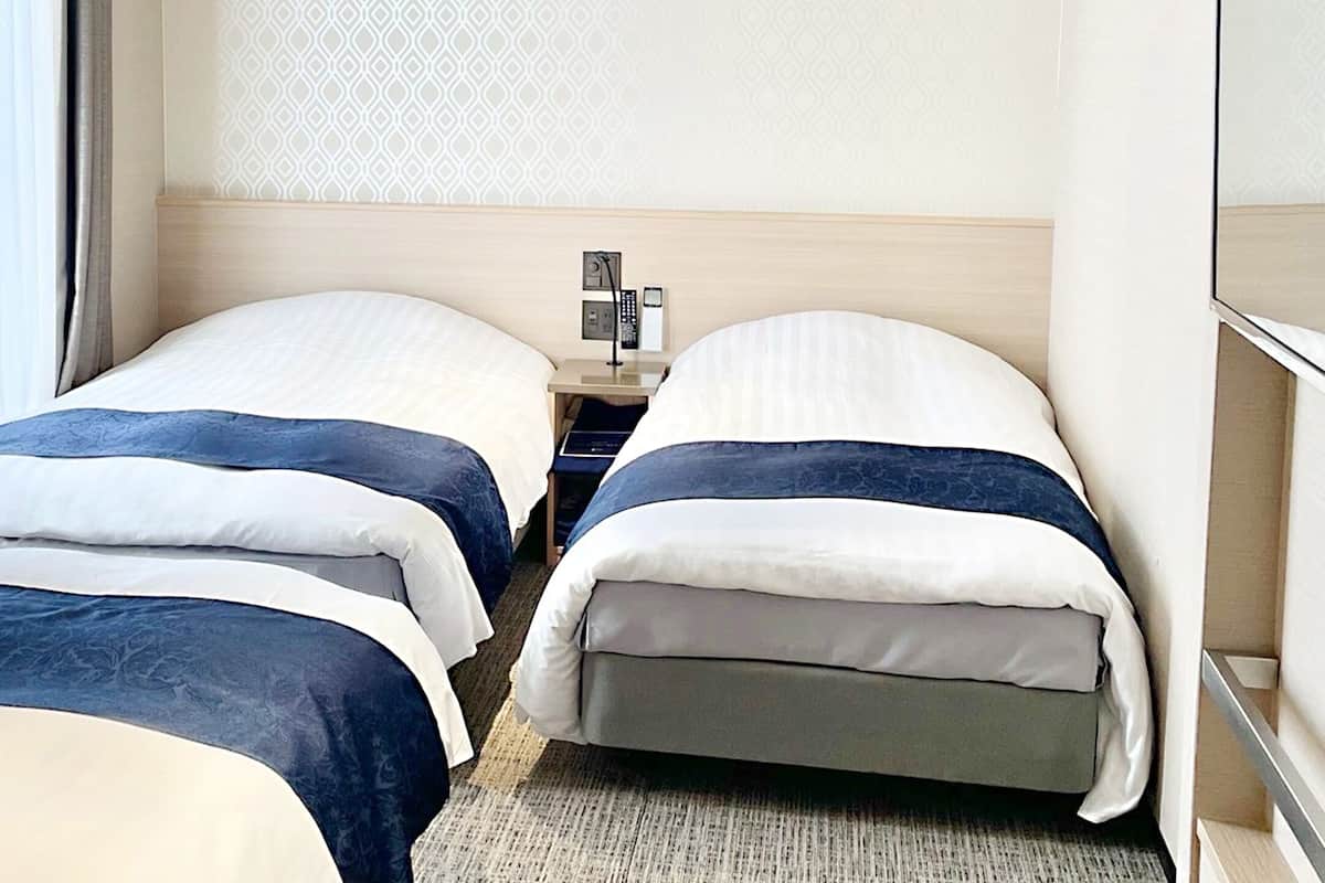 Una habitación de hotel con dos camas, una mesita de noche con lámpara y un espejo.
