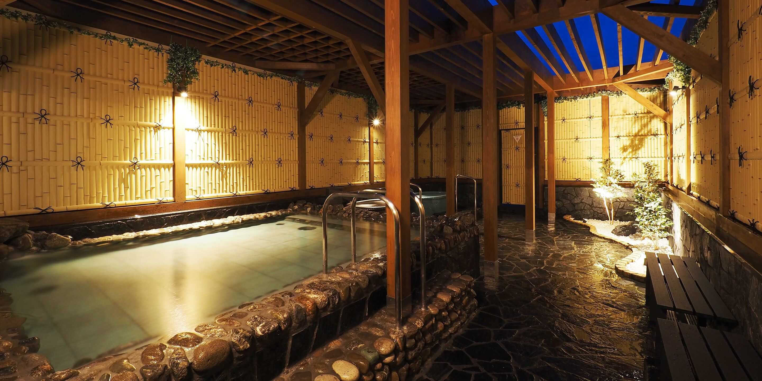 Un área de baño de aguas termales con paredes de piedra y vigas de madera, que presenta una piscina revestida de piedra y bancos de madera.