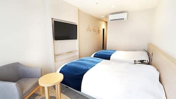 A hotel room with a bed, a chair, a small table, a TV, and an air conditioning unit.