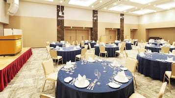 Une salle de conférence équipée de plusieurs tables rondes disposées pour un repas, d’un pupitre et d’un sol recouvert de moquette.