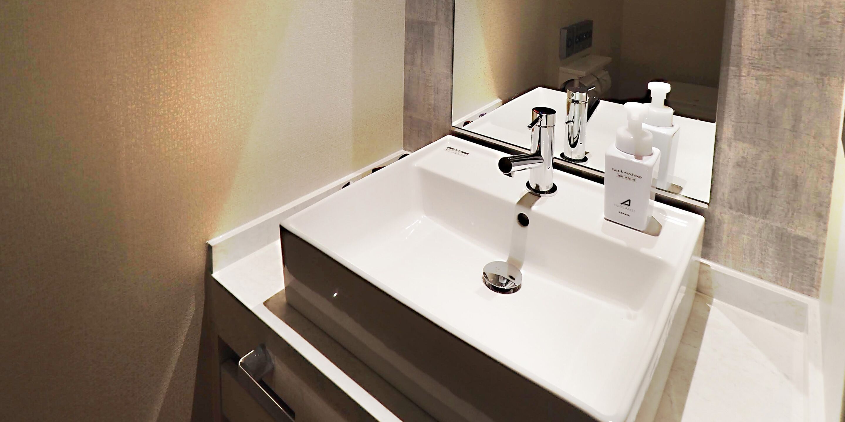 A modern bathroom with a white sink, chrome faucet, and a mirror reflecting the room.