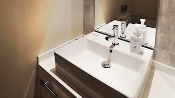 A modern bathroom with a white sink, chrome faucet, and a mirror reflecting the room.