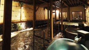 Perinteinen japanilainen onsen-kylpylä, jossa on kivilaattalattia, puurakenteita ja kuumaa lähdevettä sisältävä kylpyalue.