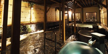 Un onsen japonés tradicional con suelo de piedra, estructuras de madera y una zona de baño de aguas termales.