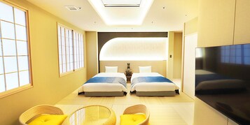 Habitación de hotel con dos camas, televisor y zona de estar con cojines amarillos.