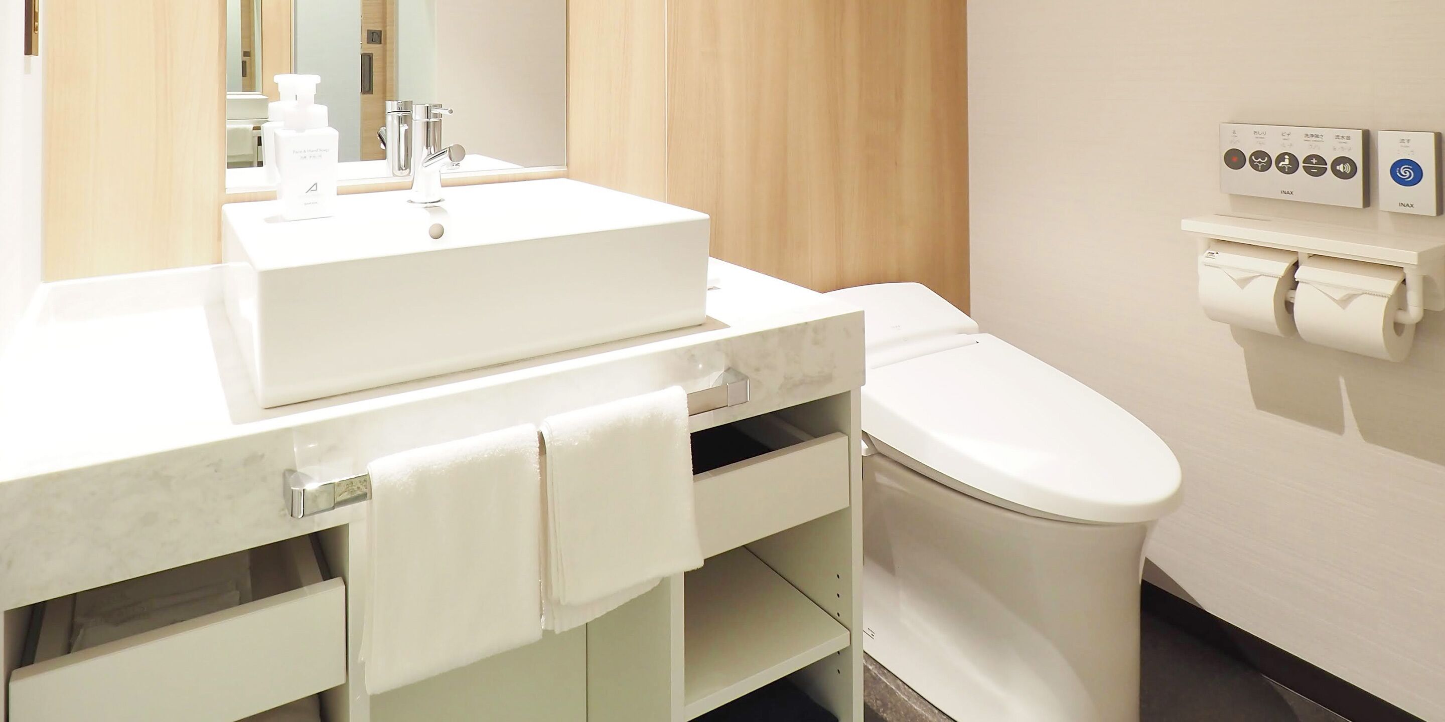 A modern bathroom with a white sink, mirror, and toilet. There are two hand dryers and a paper towel dispenser on the wall.