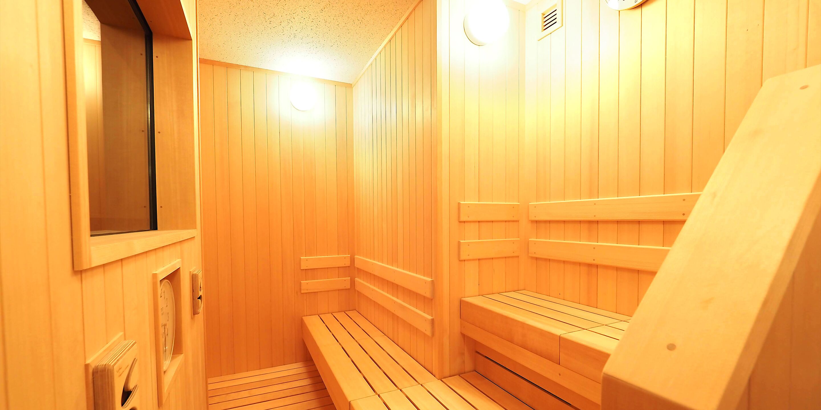 A sauna with wooden walls and benches, a clock, and a window.
