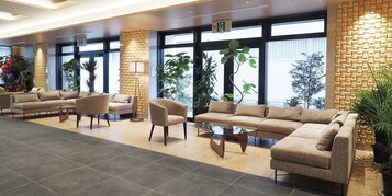 Un vestíbulo moderno con un conjunto de sofás, sillones y una mesa de centro. Se observan grandes ventanales con vistas al exterior.