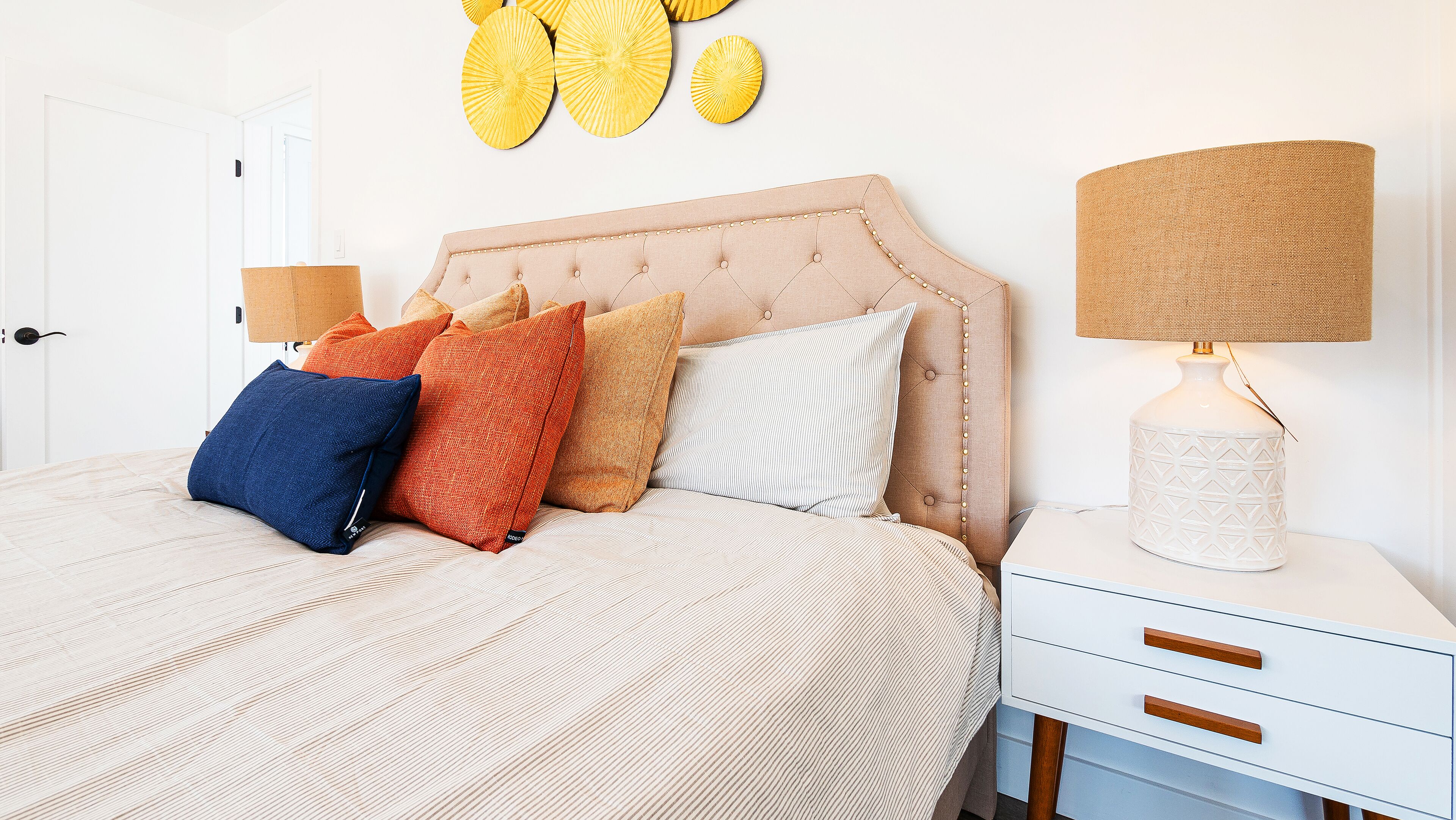 A neatly made bed with a striped bedspread, a tufted headboard, and several pillows in various colors.