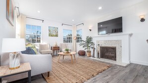 A living room with a fireplace, a television, and a large window with curtains.