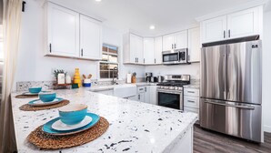 A modern kitchen with white cabinetry, stainless steel appliances, and a marble countertop.