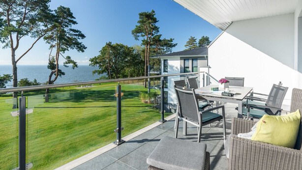 Een balkon met uitzicht op zee, buitenmeubilair en een gazon.