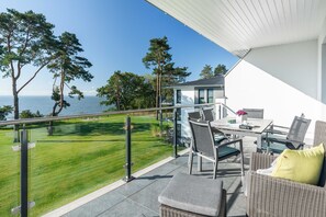 Un balcón con vista al mar, muebles de exterior y un césped.