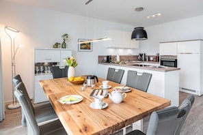 Une cuisine moderne avec des meubles blancs, une table à manger en bois et des chaises grises.
