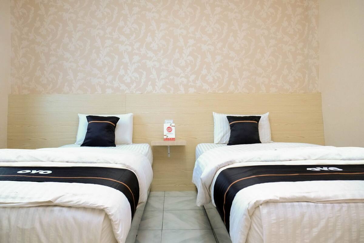 Une chambre d’hôtel avec deux lits, chacun doté d’une tête de lit, d’une petite table de chevet et d’une étagère murale sur laquelle se trouve une bouteille.