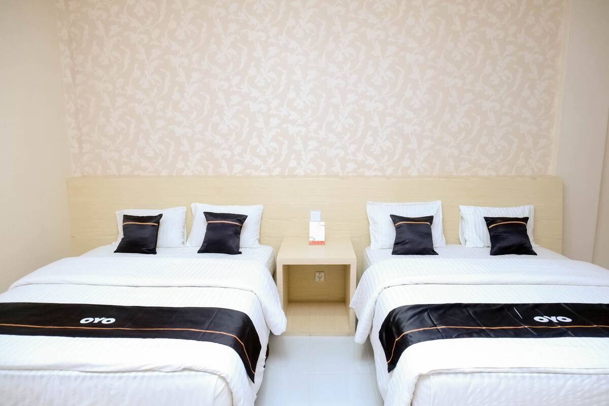 Une chambre d’hôtel avec deux lits, chacun doté de draps blancs et d’éléments décoratifs noirs, d’une tête de lit en bois et d’un papier peint à motifs.