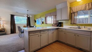 A kitchen with a large island, light-colored cabinets, and a window with curtains. - Quaint & Cozy Cottage: 3 Mi to Palisade Wineries! (Grand Junction)