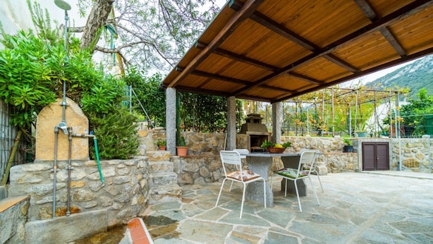 An outdoor patio with stone flooring, a wooden pergola, a stone wall, and a barbecue grill.