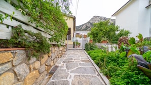 A stone pathway leading to a gate, surrounded by lush greenery and a mountain in the background.
