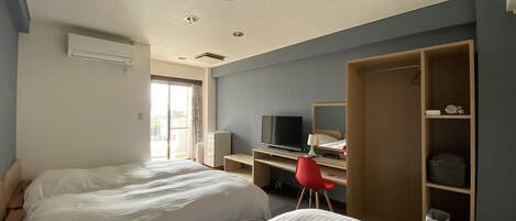A hotel room with two beds, a desk with a television, a wardrobe, and a window with curtains.