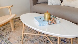 Uma sala de estar com um sofá, uma mesa de centro redonda, uma grande planta verde e um quadro na parede.