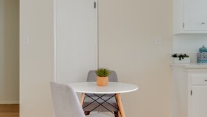 Uma área de refeições com uma mesa redonda, uma cadeira estofada cinza, um vaso de planta e um moderno lustre.