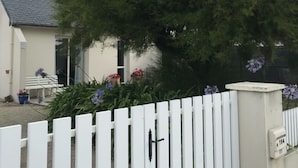 A white picket fence, a white bench, and a tree with purple flowers in front of a building. - 50m from the sea Holiday house for 2 people in Dossen (Santec)