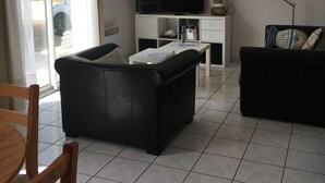 A living room with a black sofa, a white coffee table, a TV, and a lamp. There is a sliding glass door leading to an outdoor area. - 50m from the sea Holiday house for 2 people in Dossen (Santec)