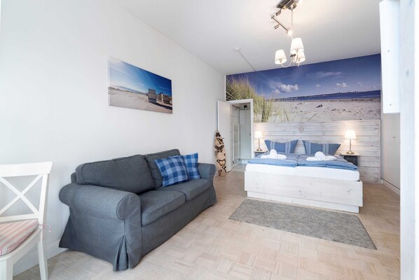 Un dormitorio moderno con una cama, un sofá gris, una silla blanca y un mural de playa en la pared.
