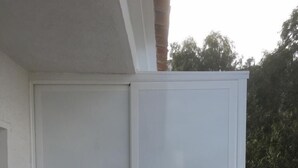 Een balkon met een witte schuifdeur en een glazen hekwerk.