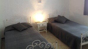 Een kamer met twee eenpersoonsbedden, een nachtkastje met een lamp en een wandlamp.