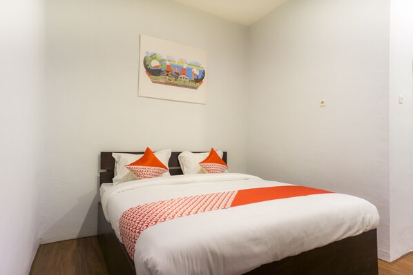 Una cama bien hecha con ropa de cama blanca y naranja, un cuadro en la pared y piso de madera.