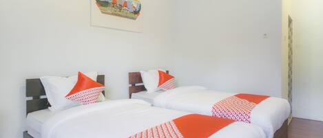Habitación de hotel con dos camas, ropa de cama blanca, detalles en naranja y una obra de arte colgada en la pared.