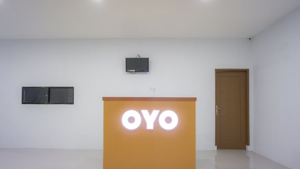 Uma área de recepção com um pódio exibindo o nome "OYO" e uma televisão fixada na parede.