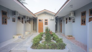 Um pátio central com jardim, rodeado por edifícios com várias janelas e aparelhos de ar condicionado.