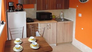 A compact kitchen with a refrigerator, microwave, and coffee maker. There is a table with four cups and saucers, and a chair.