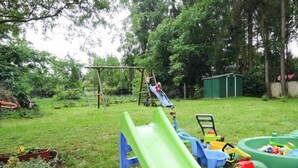 A backyard with a slide, a swing set, and a small shed.