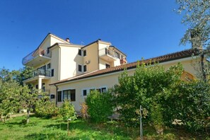 A two-story building with balconies, surrounded by greenery.