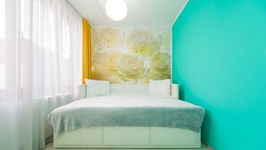 Un dormitorio con cama, pared con un mural floral, ventana con cortinas traslúcidas y una pared de acento color verde azulado.