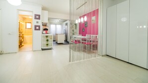 Una cocina moderna con armarios blancos, una pared de acento rosa y un comedor con sillas blancas.