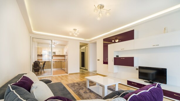 A modern living room with a sofa, coffee table, TV, and a kitchen in the background. - Relax Apartment Coresi Mall (Brasov)