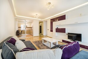 A modern living room with a sofa, coffee table, TV, and a kitchen in the background. - Relax Apartment Coresi Mall (Brasov)