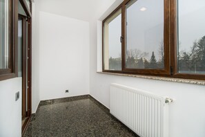 Une pièce dotée d’une grande fenêtre, de murs blancs, d’un radiateur et d’un plancher foncé à motifs.