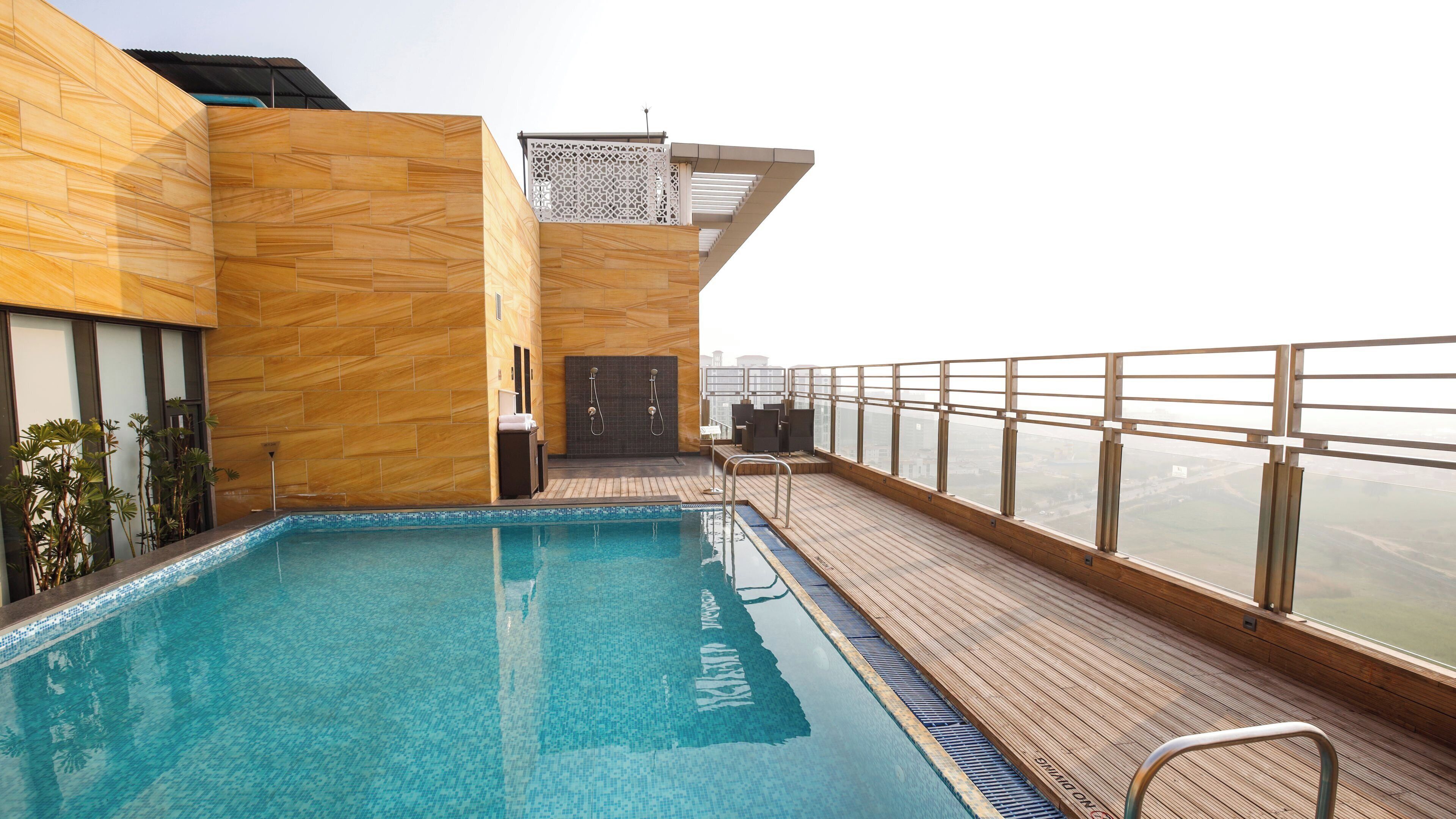 Piscina en la azotea con cubierta de madera, barandilla de vidrio y vista panorámica de la ciudad.